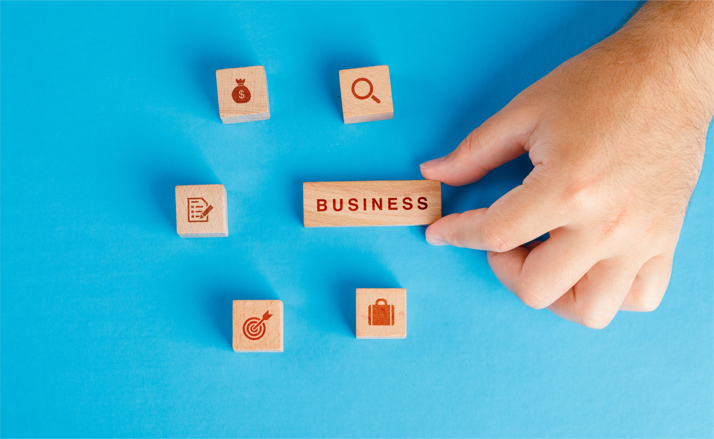 business-concept-with-icons-wooden-cubes-blue-table-flat-lay-hand-holding-wooden-block | botkeeper