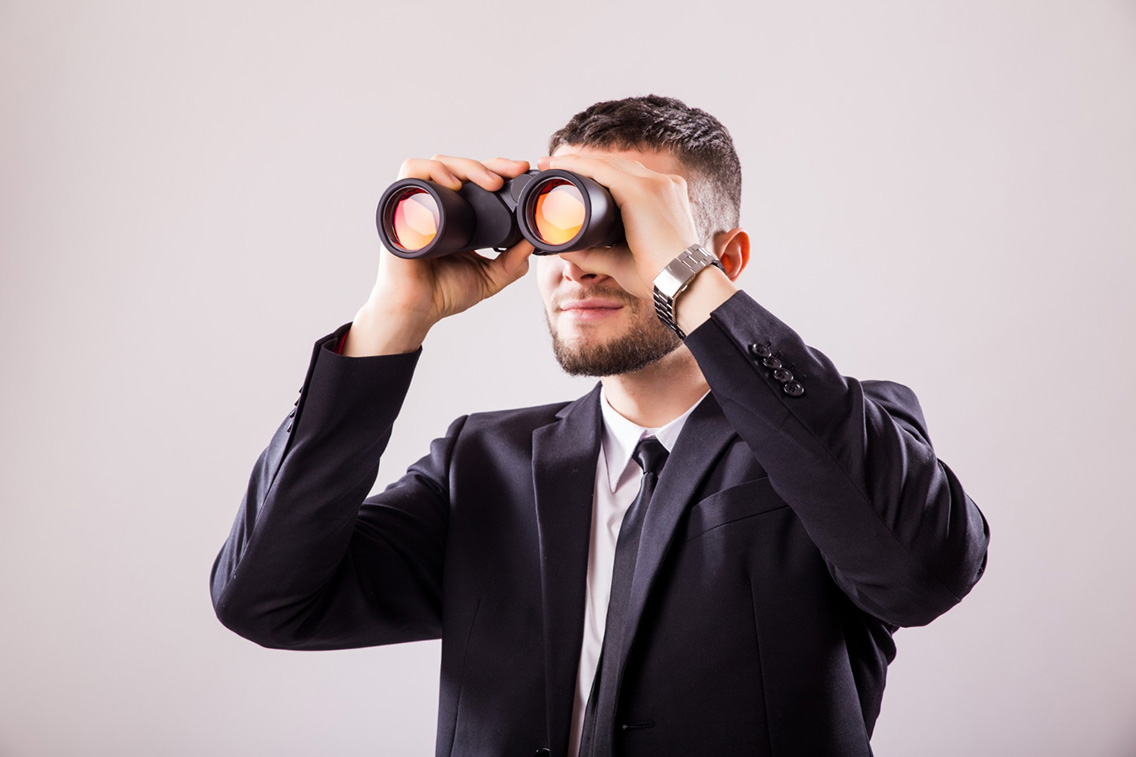 businessman-looking-through-binoculars-isolated-white-wall-botkeeper