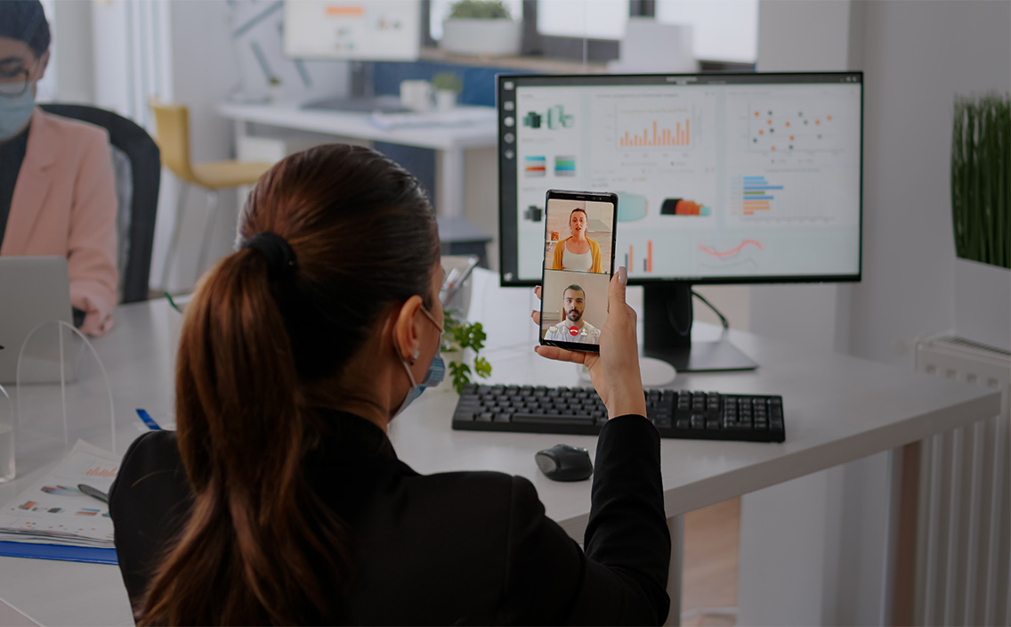 executive-business-woman-wearing-protective-face-mask-using-phone-online-videocall-conference-with-remotely-team-coworkers-working-background-respecting-social-distance-botkeeper3