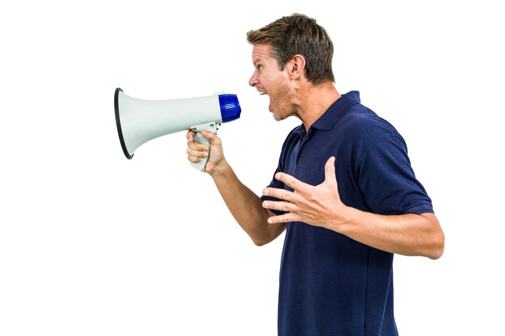 Side view of angry man shouting through megaphone against white background