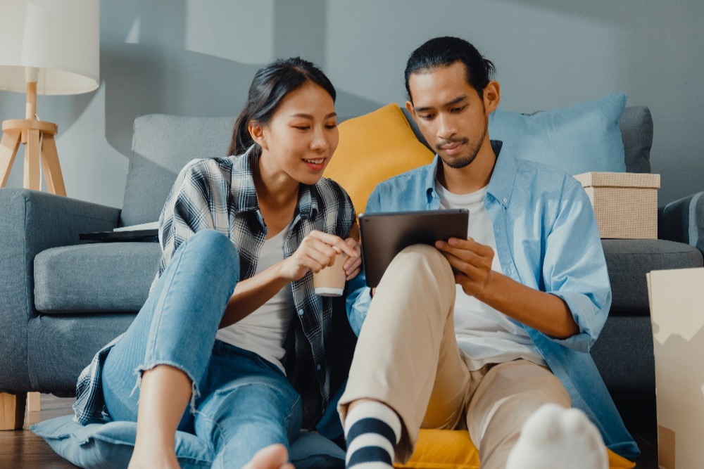 happy-asian-young-couple-man-woman-use-tablet-online-shopping-furniture-decorate-house-with-carton-packages-new-house-1-1