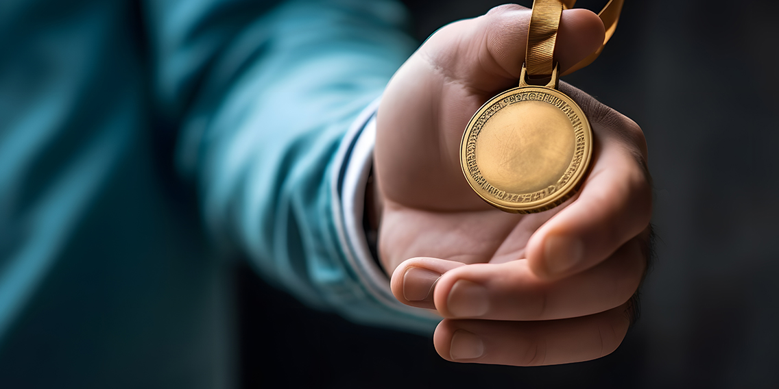 someone-holding-gold-medal-their-hand-with-blue-shirt