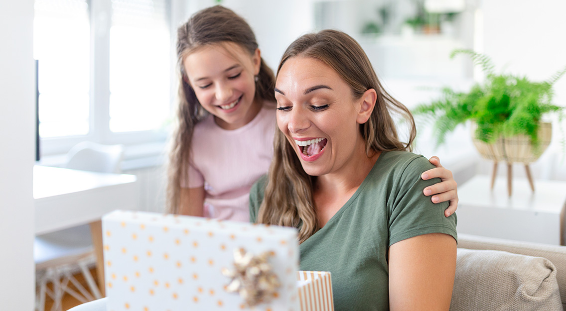 day-sitting-sofa-daughter-hugging-mom-laughing-joyful-holding-gift-box