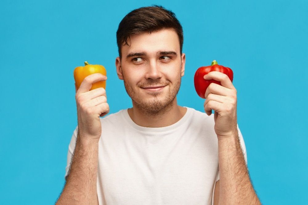 isolated-image-cute-attractive-young-man-having-thoughtful-mysterious-facial-expression-looking-away-holding-two-bell-peppers-thinking-what-cook-vegetarian-dinner-comparing-1-1